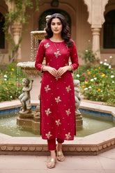 Woman in a red traditional Kurta outfit standing in front of a fountain with decorative elements. A kurta by Umaid couture