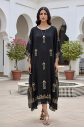 Woman wearing a black kaftan by Umaid Couture with gold patterns in an outdoor setting