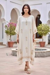 Woman in a long, light-colored dress standing in an outdoor setting with arches and plants. Product by Umaid Couture.