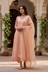 Woman in a peach traditional kurta standing in an ornate architectural setting with floral decorations. Product by Umaid Couture