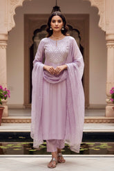 Woman in a light purple traditional outfit standing in an elegant indoor setting. Product by Umaid Couture