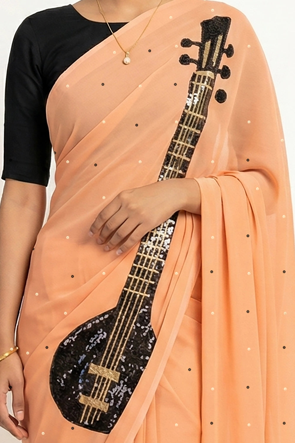 An Indian woman in peach Ragini Saree embellished with Sitar Motifs made of Zari & sequins by craft of Aari-Zardosi, a product of Umaid Couture