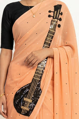 An Indian woman in peach Ragini Saree embellished with Sitar Motifs made of Zari & sequins by craft of Aari-Zardosi, a product of Umaid Couture