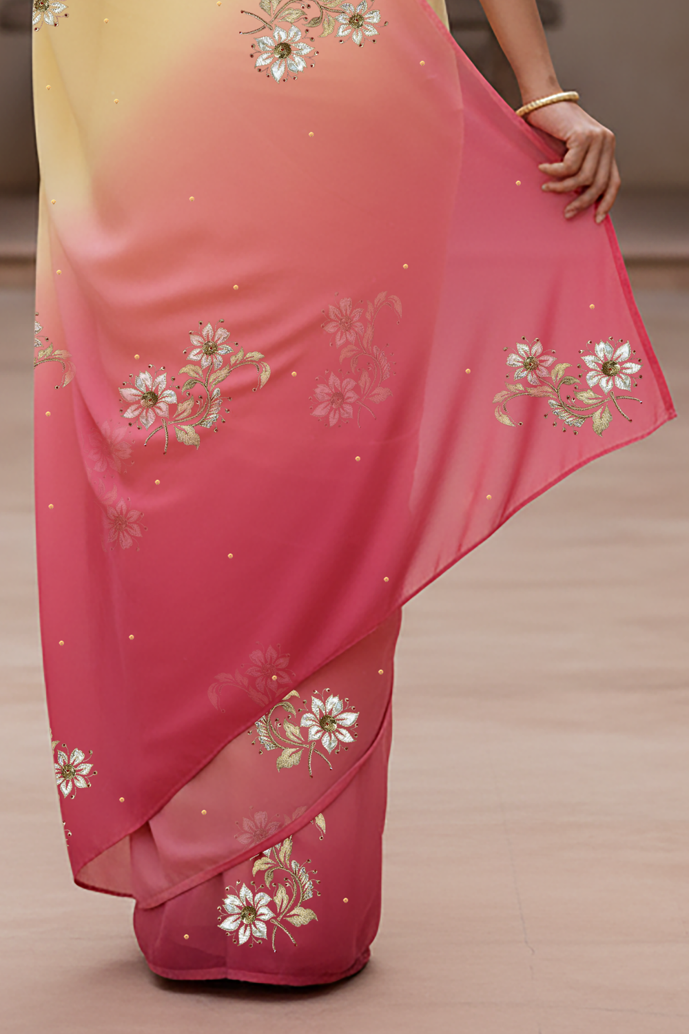 Woman wearing a yellow and pink saree by Umaid Couture with floral patterns indoors.