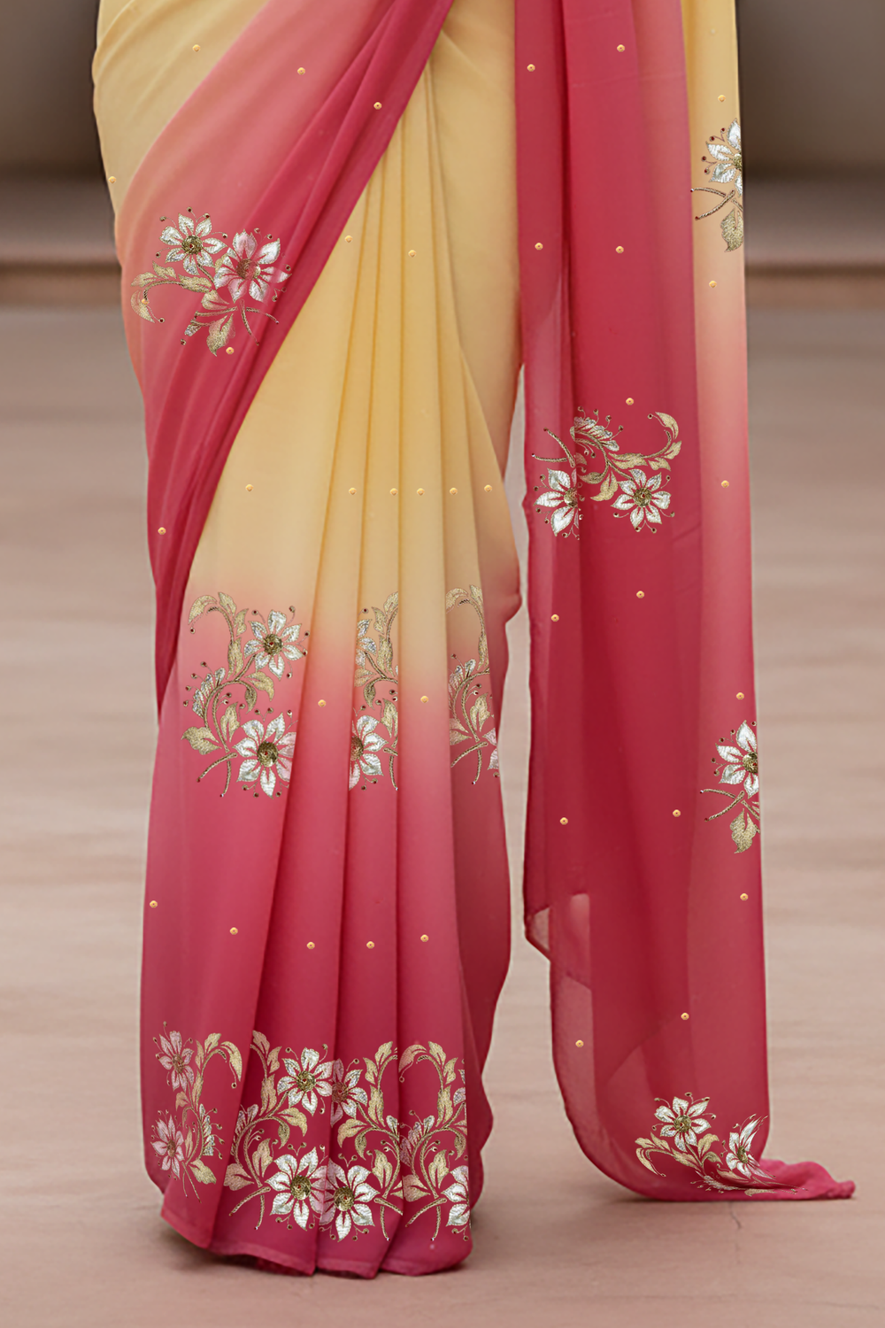 Woman wearing a yellow and pink saree by Umaid Couture with floral patterns indoors.