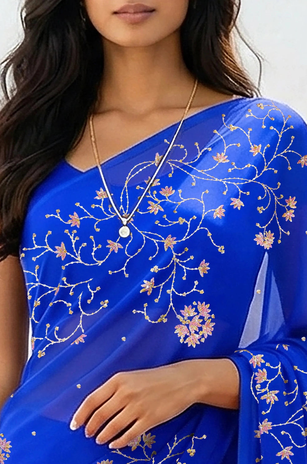 An Indian woman standing in a minimal white courtyard wearing a royal blue chiffon saree embellished with vgolden sliver and pink sequin vines of Stylized Jasmine by Umaid Couture.