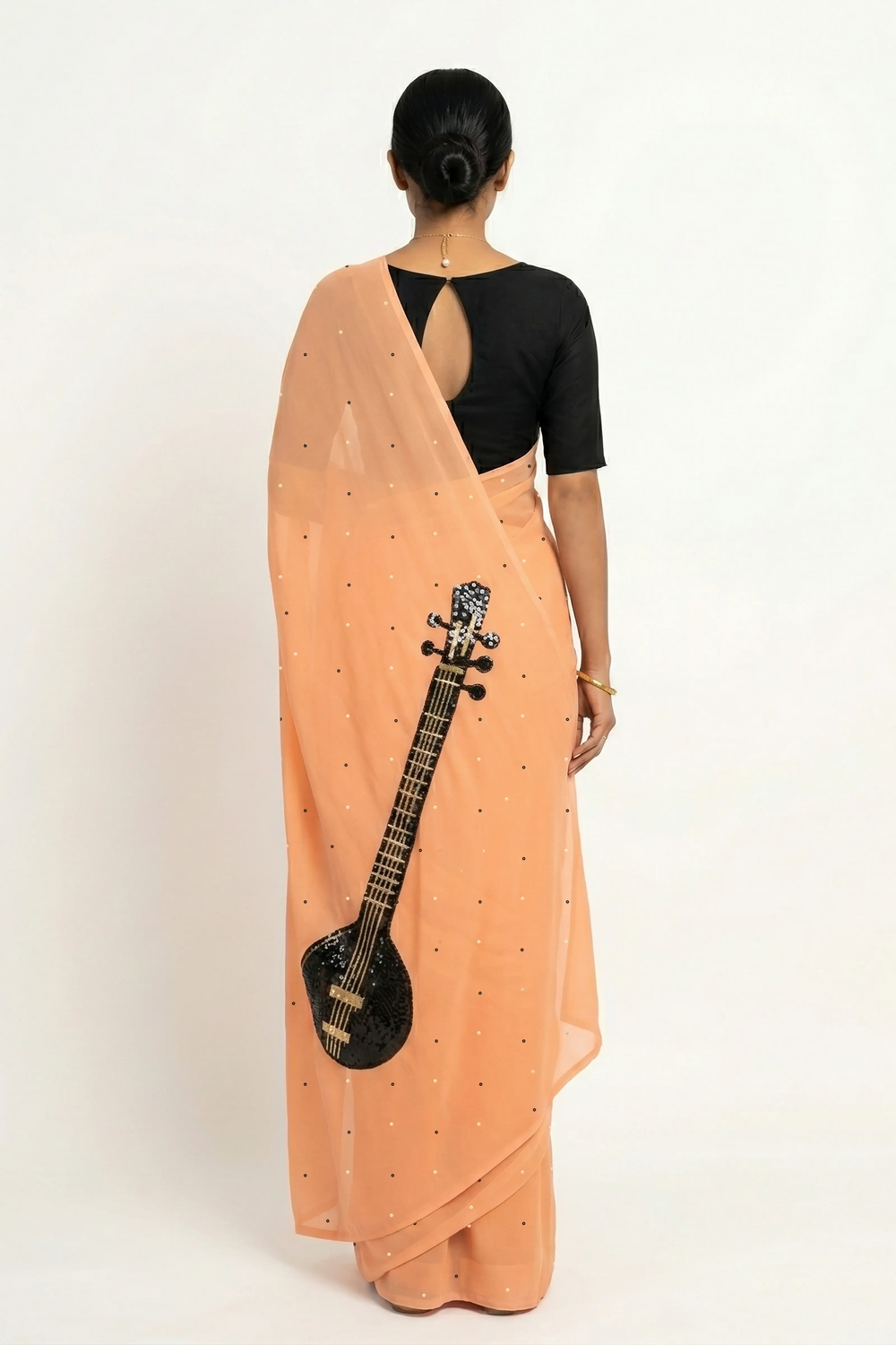 An Indian woman in peach Ragini Saree embellished with Sitar Motifs made of Zari & sequins by craft of Aari-Zardosi, a product of Umaid Couture