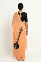 An Indian woman in peach Ragini Saree embellished with Sitar Motifs made of Zari & sequins by craft of Aari-Zardosi, a product of Umaid Couture