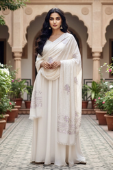 Woman wearing an off white pashmina shawl with sequins embroidery by Umaid Couture, standing in a garden courtyard.
