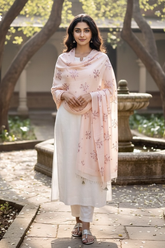 Woman wearing a pastel pink pashmina shawl embellished with sequins flowers Aari-Taari embroidery by Umaid Couture standing in a Garden Courtyard