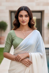 Woman wearing a green blouse and white saree with a blurred background. product by Umaid Couture