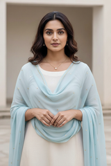 Woman wearing a light blue shawl over a white outfit with a neutral background. product by Umaid Couture