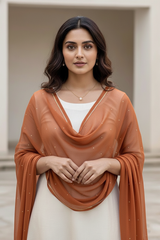Woman wearing a rust-colored dupatta over a white outfit, standing against a neutral background. product by Umaid Couture