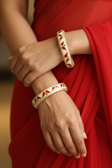 Close-up of a person wearing two red and gold bangles on a blurred red fabric background