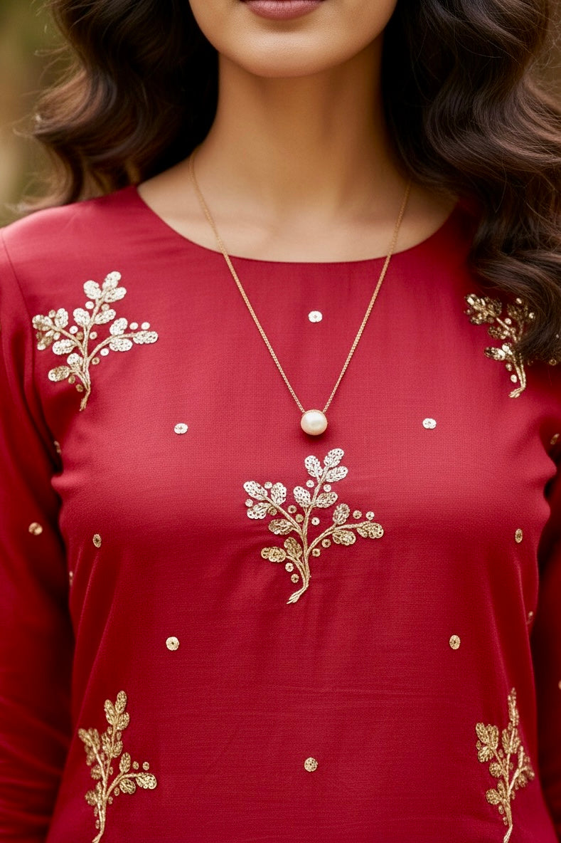 Red top with gold floral embroidery and a necklace worn by a person.