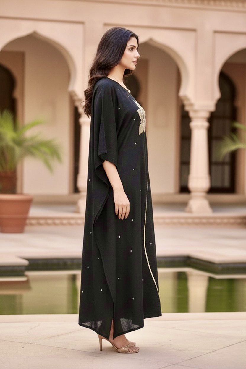 Woman in a black dress standing in an outdoor setting with arches and plants. Product by Umaid Couture