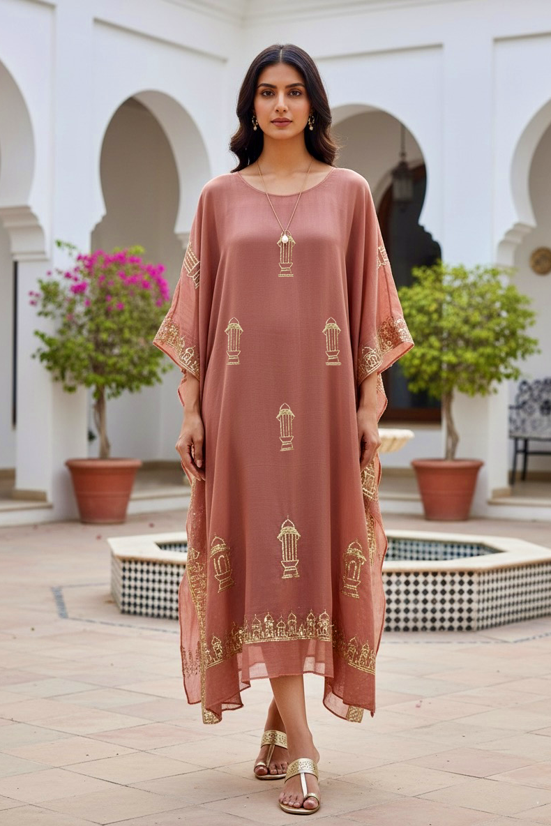 Woman in a long, light pink embroidered kaftan by Umaid Couture standing in a courtyard with arches and plants.