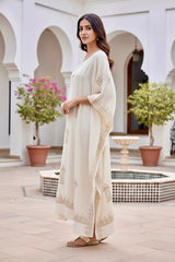 Woman in a white traditional outfit standing in a courtyard with arches and plants. product by Umaid Couture.