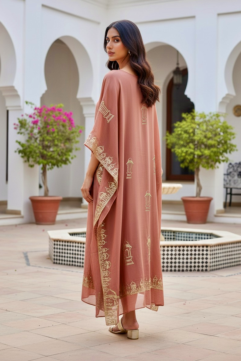 Woman in a long, light pink embroidered kaftan by Umaid Couture standing in a courtyard with arches and plants.