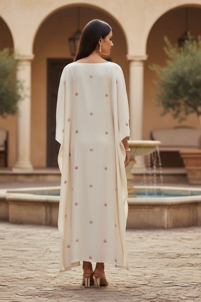 Woman in a long, light-colored kaftan standing in a courtyard with arches and a fountain. Product by Umaid Couture