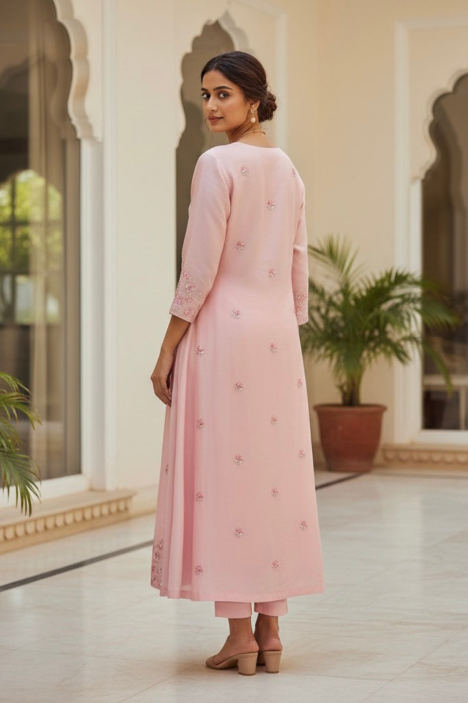 Woman in a pink kurta standing in an elegant indoor setting with plants . Product by Umaid Couture