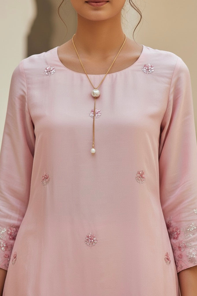 Pink embroidered dress with a necklace on a neutral background. Product by Umaid Couture