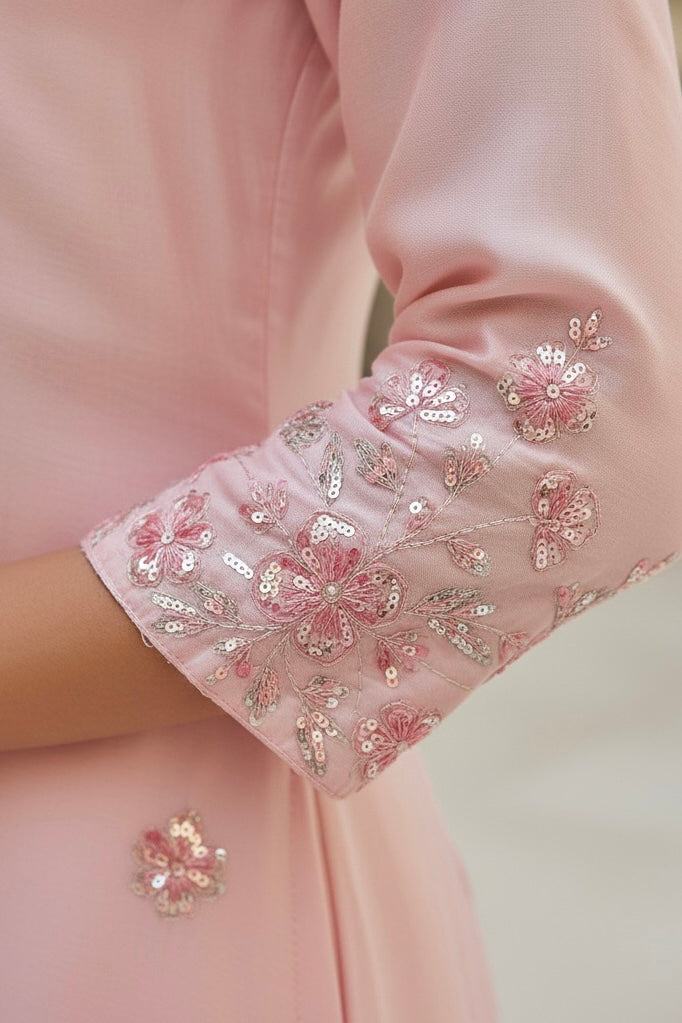 Close-up of a pink garment with floral embroidery on a blurred background. Product by Umaid Couture