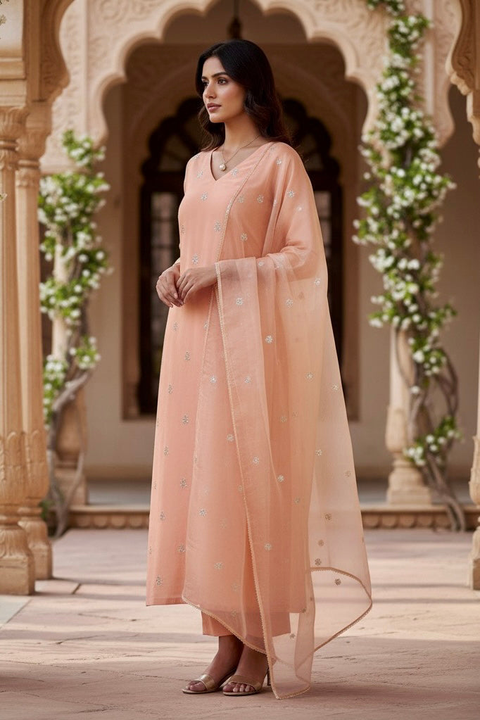 Woman in a peach traditional outfit standing in an ornate architectural setting with floral decorations. Product by Umaid Couture