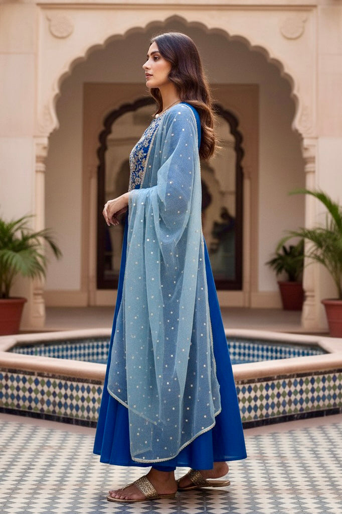 Woman in a blue traditional outfit with a light blue dupatta standing in front of an archway. Product by Umaid Couture