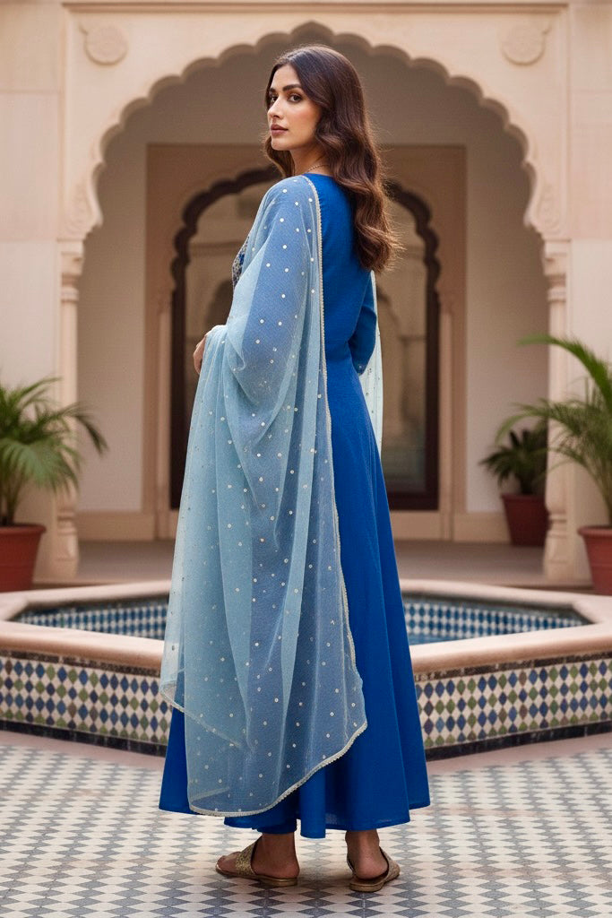 Woman in a blue traditional outfit standing in front of an archway with plants. Product by Umaid Couture