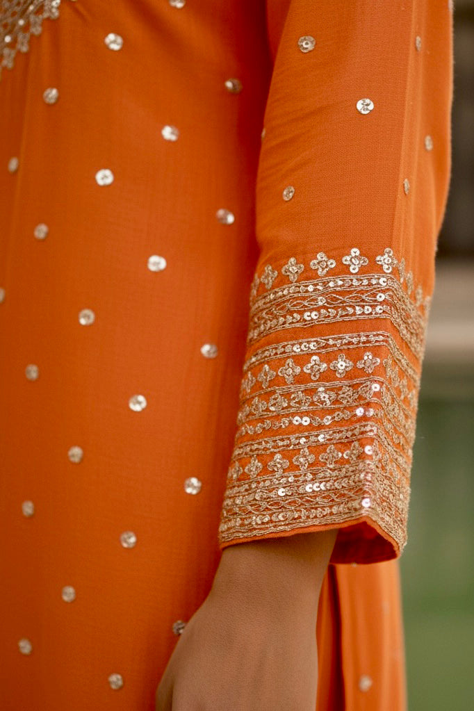 Close-up of an orange garment with intricate silver embroidery. Product by Umaid Couture