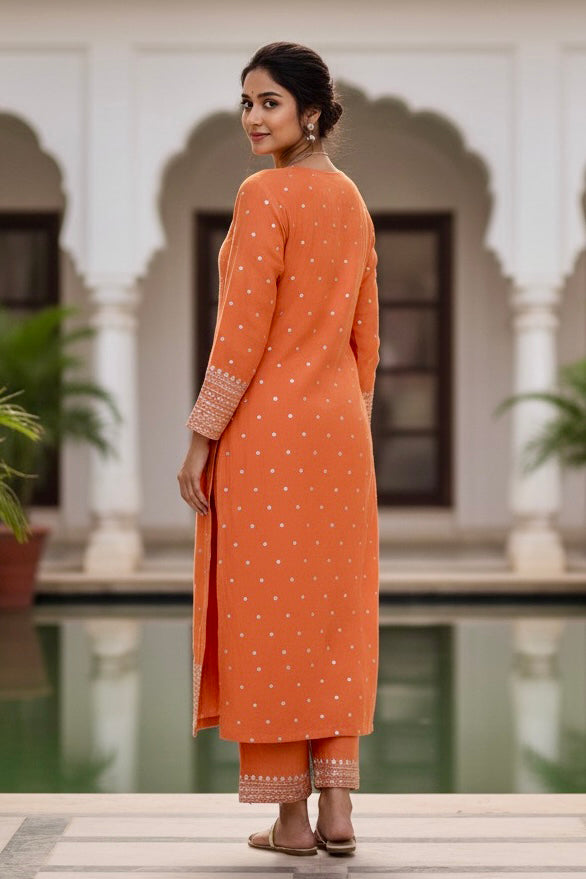 Woman in an orange traditional outfit standing by a pool with white arches in the background. Product by Umaid Couture