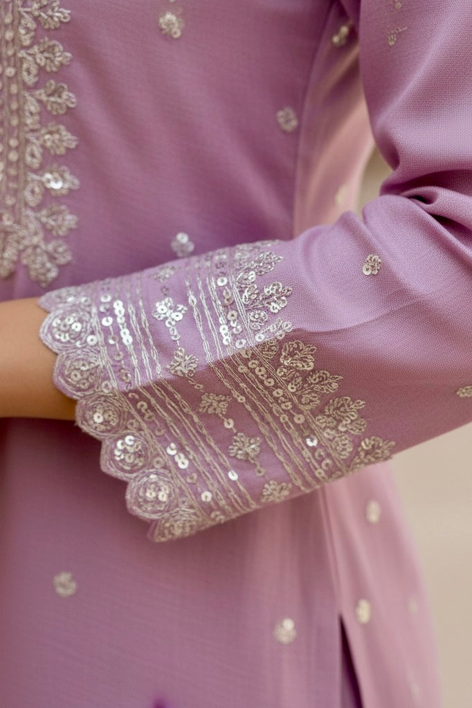 Close-up of a pink garment with intricate gold embroidery on a blurred background. Product by Umaid Couture