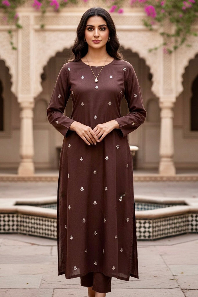 Woman wearing a brown dress with white patterns in an outdoor setting with arches and flowers. Product by Umaid Couture