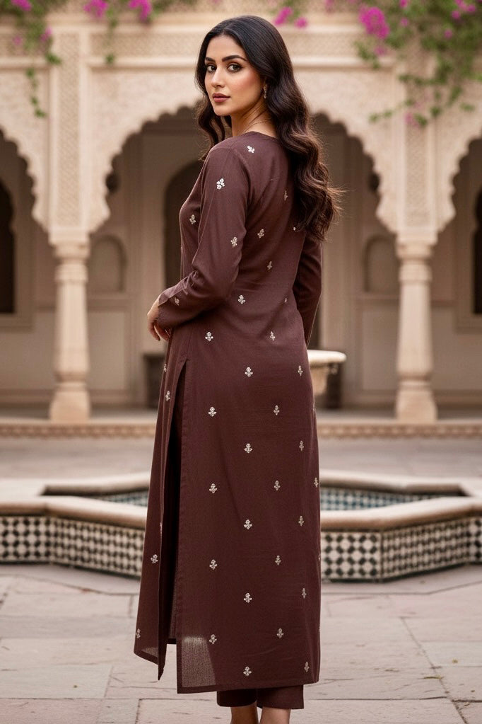 Woman in a brown traditional outfit standing in front of an architectural background with arches and columns. Product by Umaid Couture