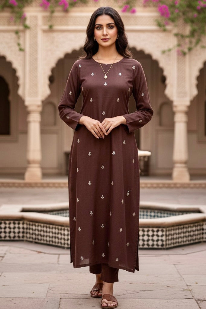 Woman wearing a brown kurta with white patterns in an outdoor setting with architectural elements. Product by Umaid Couture