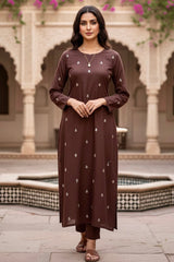 Woman wearing a brown kurta with white patterns in an outdoor setting with architectural elements. Product by Umaid Couture