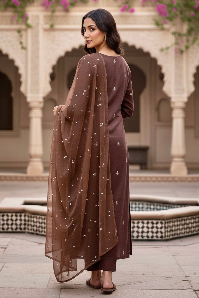 Woman in a brown traditional kurta standing in an architectural courtyard. Product by Umaid Couture