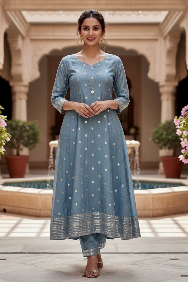 Woman in a blue Kurta standing in a courtyard with columns and plants. Product by Umaid Couture