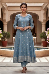 Woman in a blue Kurta standing in a courtyard with columns and plants. Product by Umaid Couture
