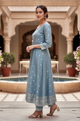 Woman in a light blue traditional outfit standing in an outdoor setting with columns and plants. Product by Umaid Couture