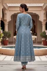 Woman in a blue traditional outfit standing in a courtyard with columns and plants. Product by Umaid Couture