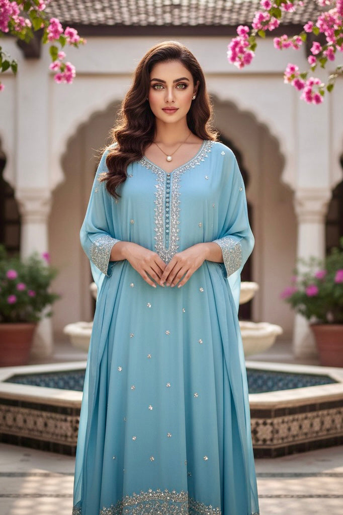 Woman in a light blue dress with intricate detailing standing in an outdoor setting with pink flowers and arches. Product by Umaid Couture