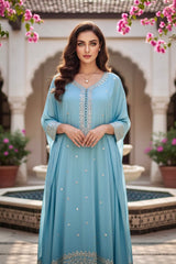 Woman in a light blue dress with intricate detailing standing in an outdoor setting with pink flowers and arches. Product by Umaid Couture