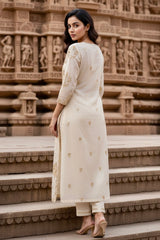 Woman in a white traditional outfit standing on steps with a temple background. Product by Umaid Couture