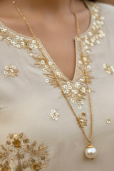 Close-up of a gold necklace with a pearl pendant on a beige embroidered garment. Product by Umaid Couture