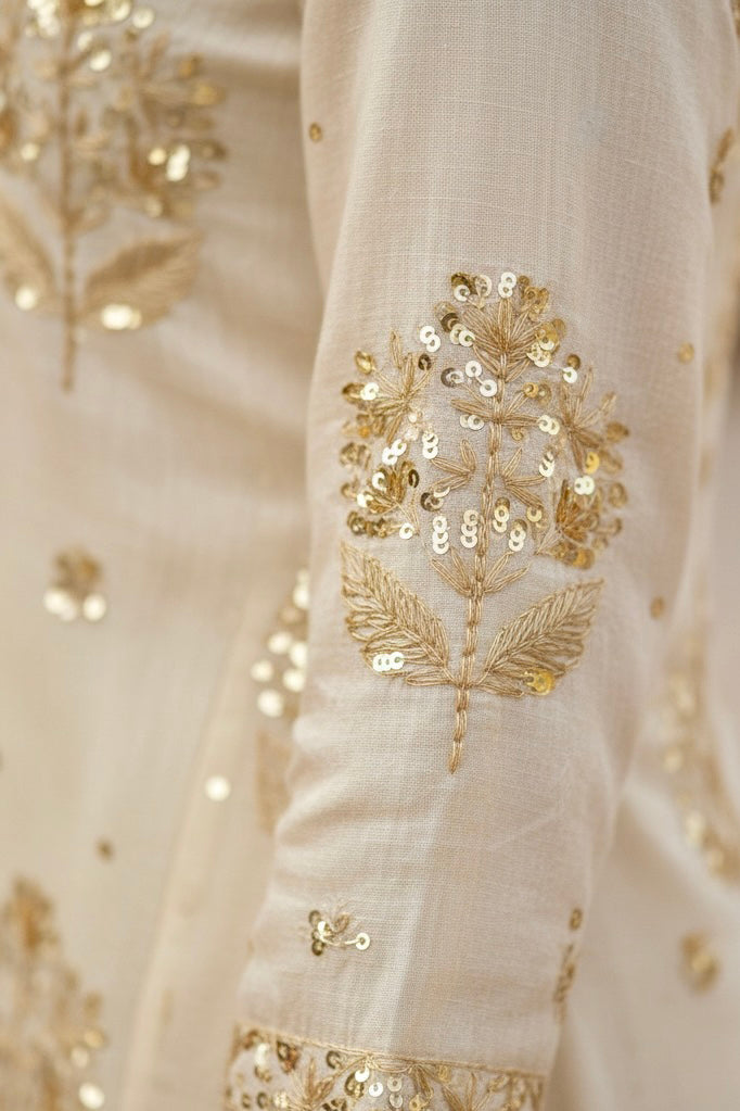 Close-up of a cream fabric with gold floral embroidery. Product by Umaid Couture