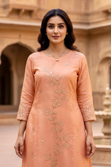 Woman wearing a peach-colored embroidered dress in an outdoor setting. Product by Umaid Couture