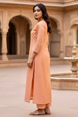Woman in peach traditional outfit standing in a courtyard with arches and a fountain. Product by Umaid Couture