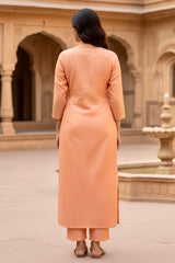 Woman wearing a peach kurta in an outdoor setting with architectural elements. Product by Umaid Couture